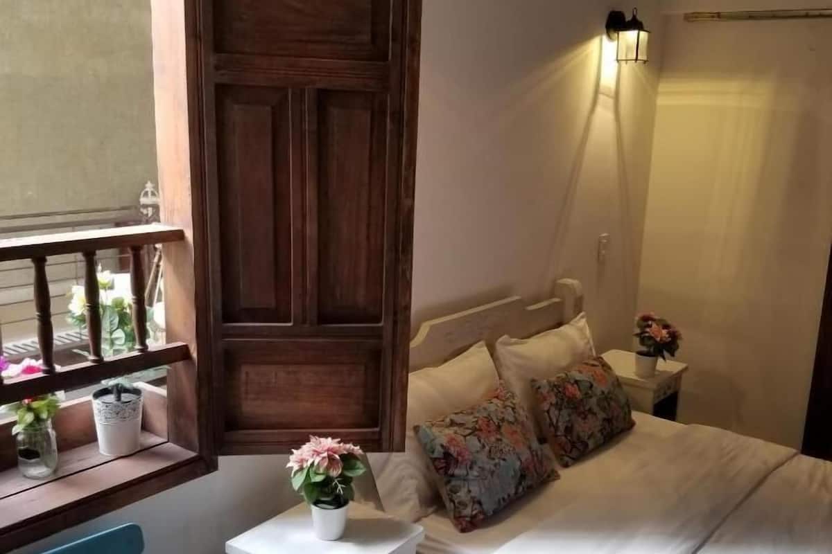 A bedroom with a bed, bedside table, lamp, window, and a small cabinet.