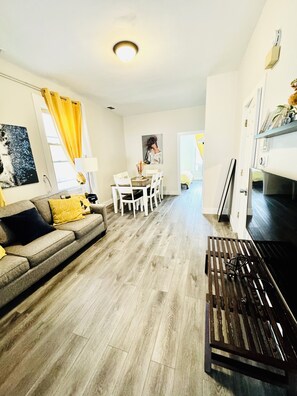 Ein modernes Wohnzimmer mit einer Couch, einem Esstisch, Stühlen und einer Küchenzeile mit Kühlschrank und Mikrowelle.