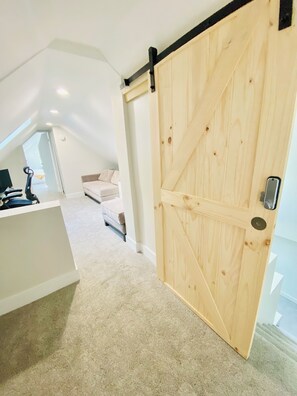 Ein Schlafzimmer mit einer großen Holztür, einem weißen Bett und einem Schreibtisch mit einem Computer.