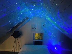 Ein Dachzimmer mit geneigter Decke, einem Sternprojektor, Kunstwerken und einem Aquarium.
