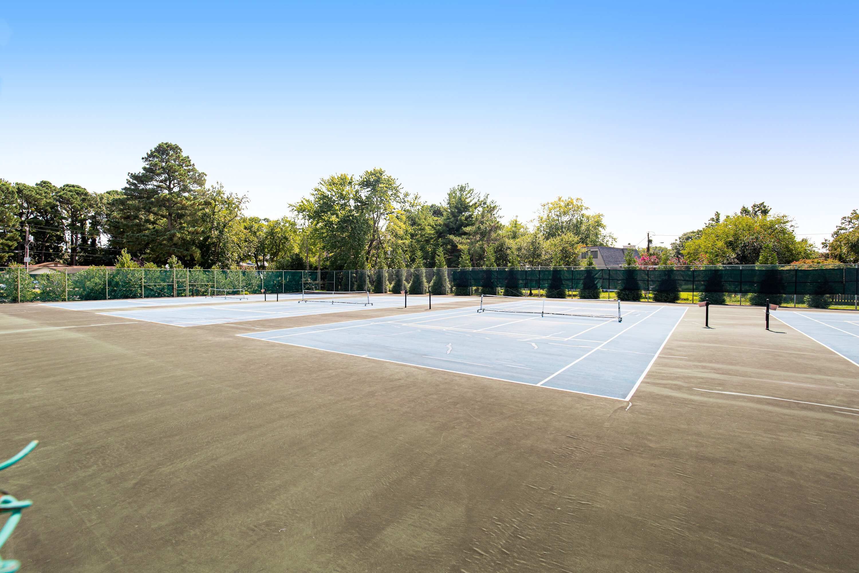 A tennis court with a net, surrounded by trees and a fence.
