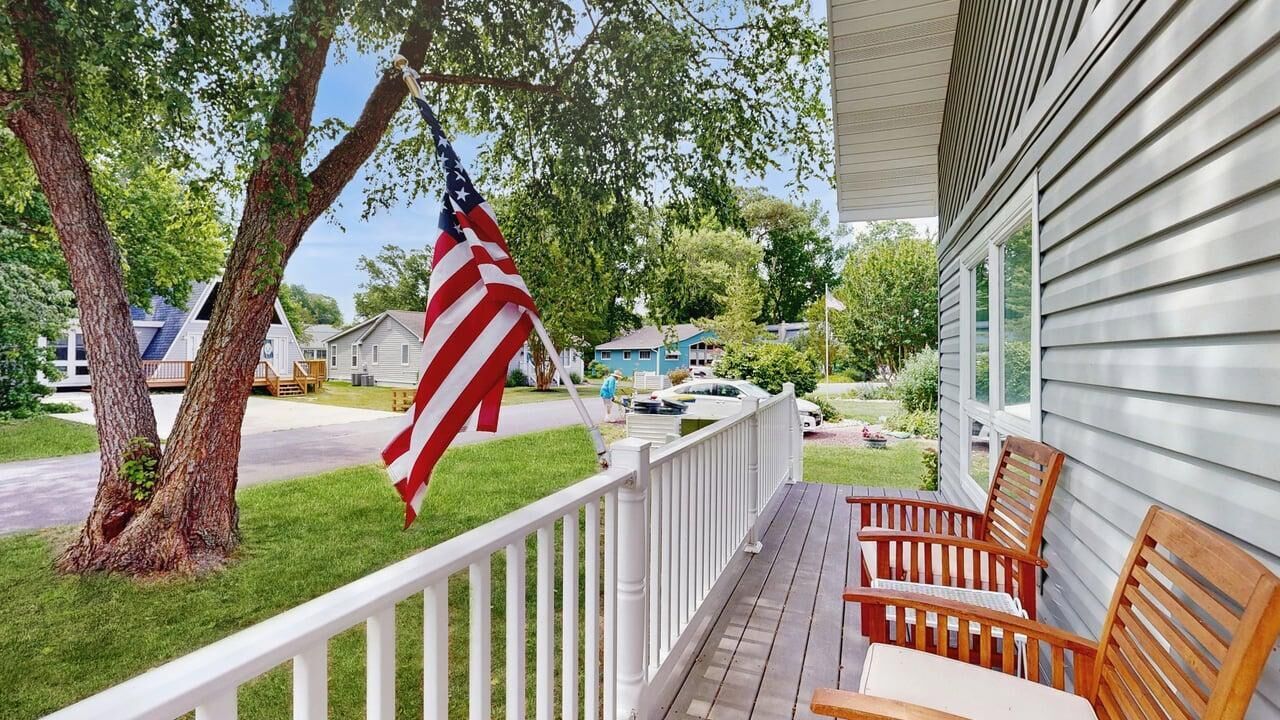 A porch with a white railing, wooden chairs, and an American flag.