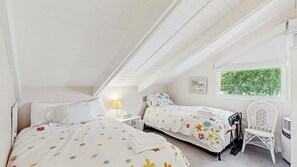 Ein Schlafzimmer mit zwei Betten, einem Fenster, einem Sessel und einem Nachttisch.