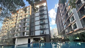 A modern apartment building with a swimming pool, outdoor seating, and balconies.