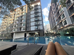 A modern apartment building with a swimming pool, outdoor seating, and balconies.