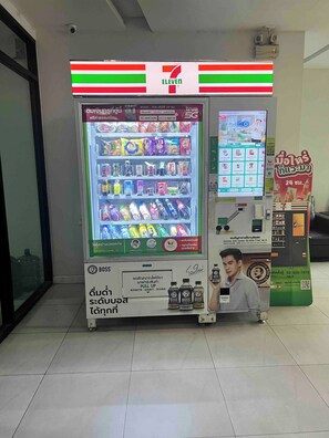 A 7-Eleven convenience store with a refrigerated beverage display, a coffee machine, and a digital menu screen. - Living Avenue Condominuim (Chonburi)