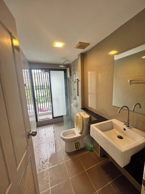 A bathroom with a toilet, sink, shower, and a glass door leading to a balcony. - Living Avenue Condominuim (Chonburi)