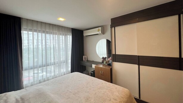 A hotel room with a bed, a dresser, a mirror, and an air conditioning unit.