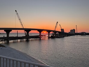 Eine Brücke mit Baukränen, einem Sonnenuntergang und ruhigem Wasser.