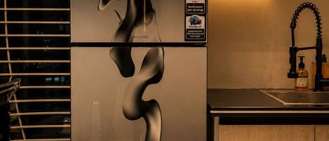 Una cocina moderna con un refrigerador de acero inoxidable que presenta un diseño en espiral único, un gabinete de madera y un grifo negro.