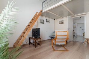 Ein Zimmer mit einer Holzleiter, einem Fernseher auf einem kleinen Tisch, einem Stuhl und einer Tür zu einem weiteren Raum.