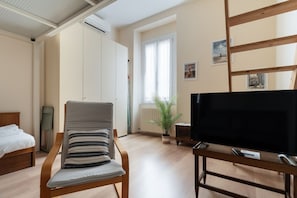 Ein Zimmer mit einem Bett, einem Sessel, einem Fernseher, einem Heizkörper und einem Vorhangfenster.