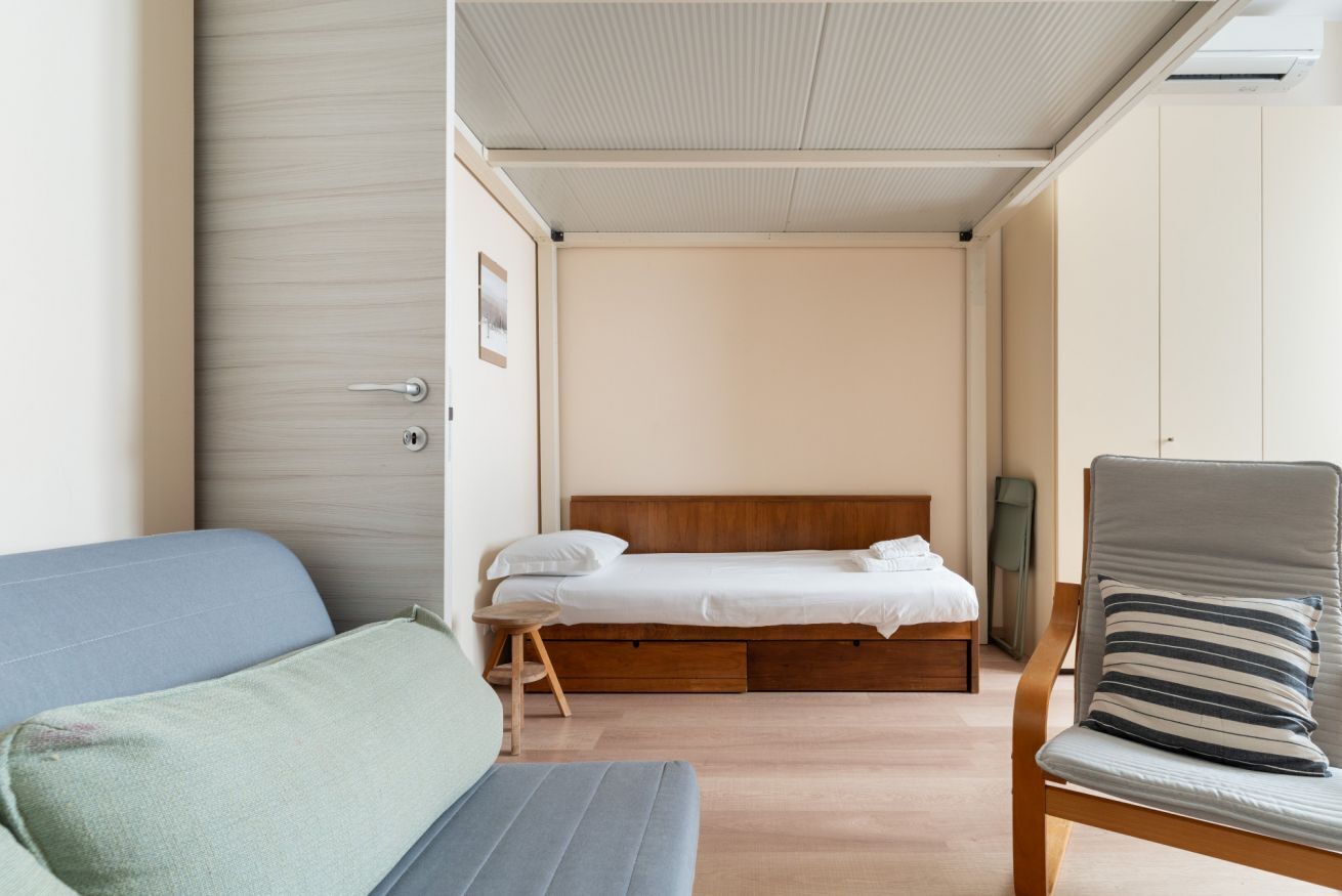 A compact bedroom with a bed, a chair, and a sofa.