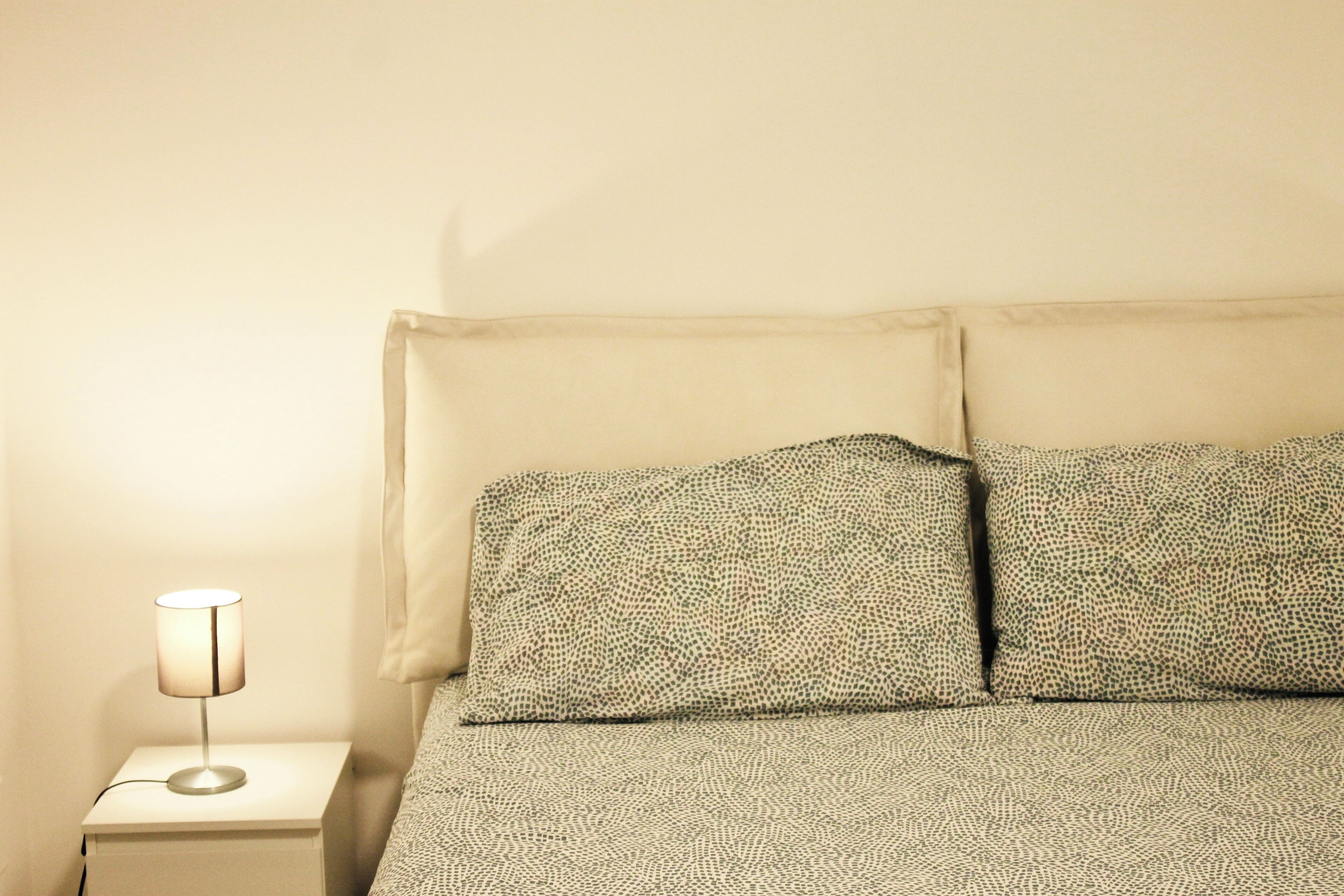 Uma cama com roupa de cama estampada, uma luminária de cabeceira e uma mesa de cabeceira branca.