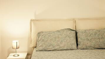 Uma cama com roupa de cama estampada, uma luminária de cabeceira e uma mesa de cabeceira branca.