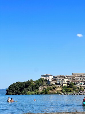 A coastal town with buildings on a hillside, a clear blue sky, and people in the water.