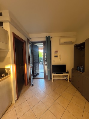A hallway leading to a balcony with a TV and a cabinet.