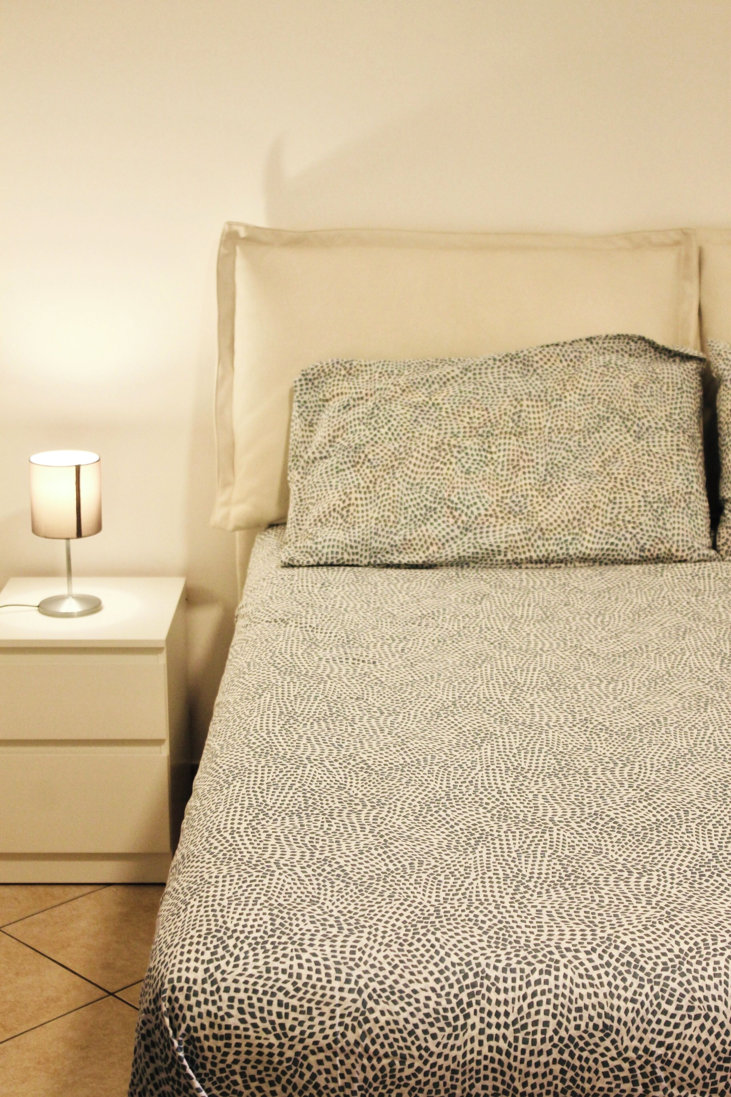 Een bed met een beddegoed met patroon, een bedlampje en een nachtkastje.