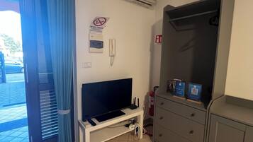 Quarto com televisão em um suporte, ar condicionado branco, extintor de incêndio e porta com cortina azul.