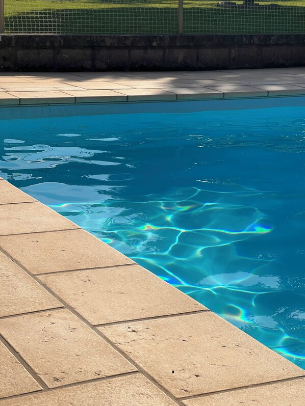 A swimming pool with clear water, a tiled edge, and a grassy area in the background.