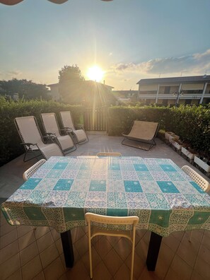 A patio with a table covered in a patterned tablecloth, surrounded by lounge chairs.