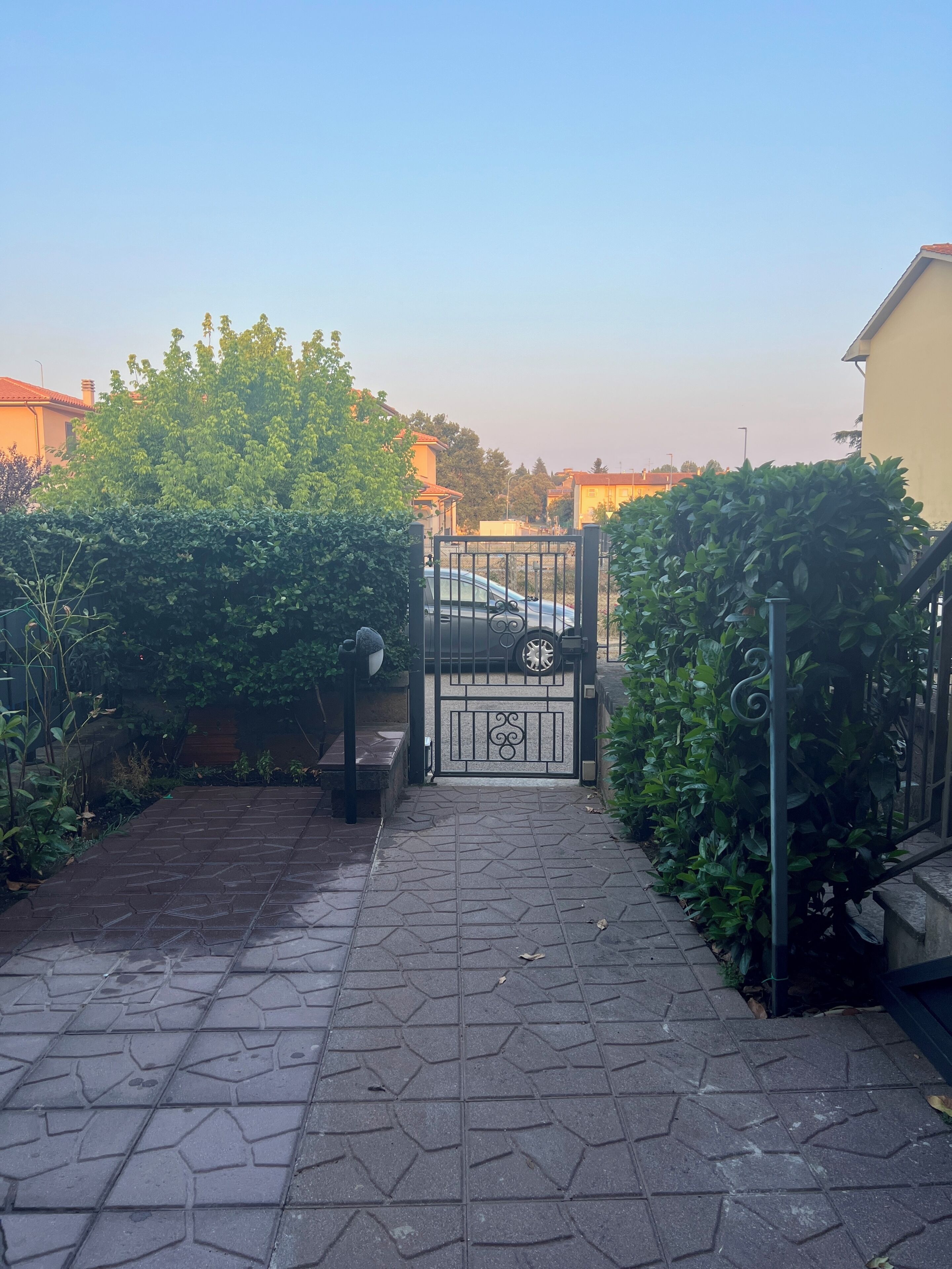 Un chemin pavé mène à une entrée fermée par un portail, à l’intérieur de laquelle se trouve un véhicule stationné.