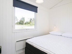 Ein Schlafzimmer mit einem Bett, einem Fenster mit Jalousie, einem Wandheizkörper und einer Nachttischlampe.