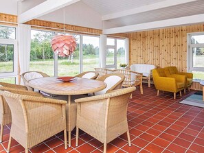 A room with a round table, wicker chairs, a yellow armchair, and a wooden wall. - 6 Person Holiday Home in Bindslev (Bindslev)