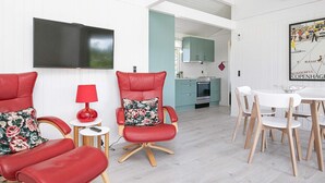 A modern living room with red leather chairs, a flat-screen TV, a dining area with white chairs, and a kitchen with teal cabinets. - 6 Person Holiday Home in Bindslev (Bindslev)