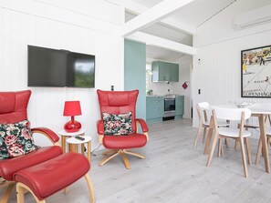 A modern living room with red leather chairs, a flat-screen TV, a dining area with white chairs, and a kitchen with teal cabinets. - 6 Person Holiday Home in Bindslev (Bindslev)