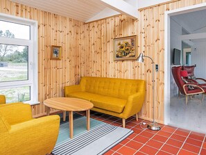 A room with a yellow sofa, a small round table, and a red chair. There are two windows and a door leading to another room. - 6 Person Holiday Home in Bindslev (Bindslev)