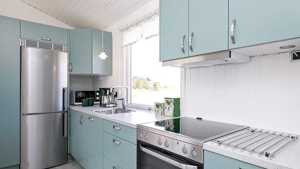 A modern kitchen with teal cabinetry, stainless steel appliances, and a large window providing natural light. - 6 Person Holiday Home in Bindslev (Bindslev)