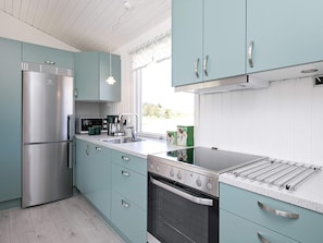 A modern kitchen with teal cabinetry, stainless steel appliances, and a large window providing natural light. - 6 Person Holiday Home in Bindslev (Bindslev)