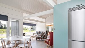 A modern kitchen with a stainless steel refrigerator, wooden dining table with chairs, and a floral sofa. - 6 Person Holiday Home in Bindslev (Bindslev)