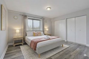 A bedroom with a bed, bedside lamps, a window with curtains, a wardrobe, and a patterned rug.