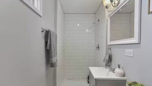 Un baño con ducha, lavabo, espejo y toallero.