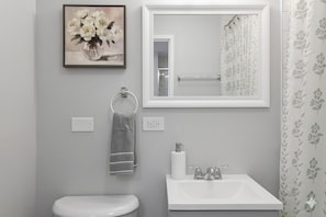 A bathroom with a toilet, sink, towel rack, mirror, and a framed floral painting.
