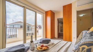 A hotel room with a large window, a bed with a patterned bedspread, a bedside table with a bottle and a tray of food, and a wooden accent wall. - Mambo Private Villa w/ Pool by the Beach (Paralimni)