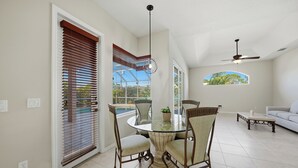 Uma sala de jantar com mesa de vidro, cadeiras, ventilador de teto e vista para o exterior.