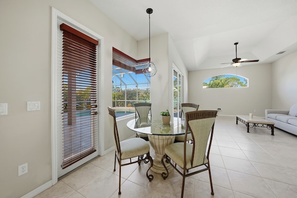A dining area with a glass table, chairs, a ceiling fan, and a view of the outdoors. - 3-bedroom house w/ Saltwater Pool in Boating community (Port Charlotte)