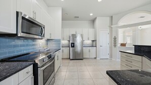 Uma cozinha moderna com eletrodomésticos de aço inoxidável, armários brancos e painel de fundo azul.