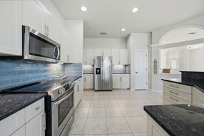 A modern kitchen with stainless steel appliances, white cabinetry, and a blue backsplash. - 3-bedroom house w/ Saltwater Pool in Boating community (Port Charlotte)