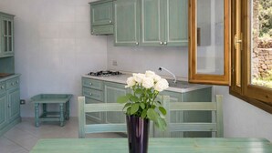 A kitchen with teal cabinets, a gas stove, a wooden table, and a vase with white flowers.