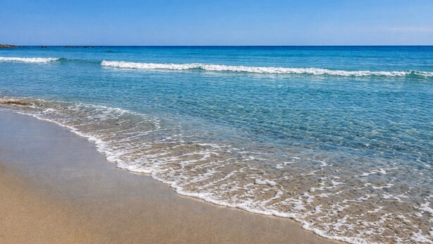 A beach with clear water, waves, and a sandy shore.