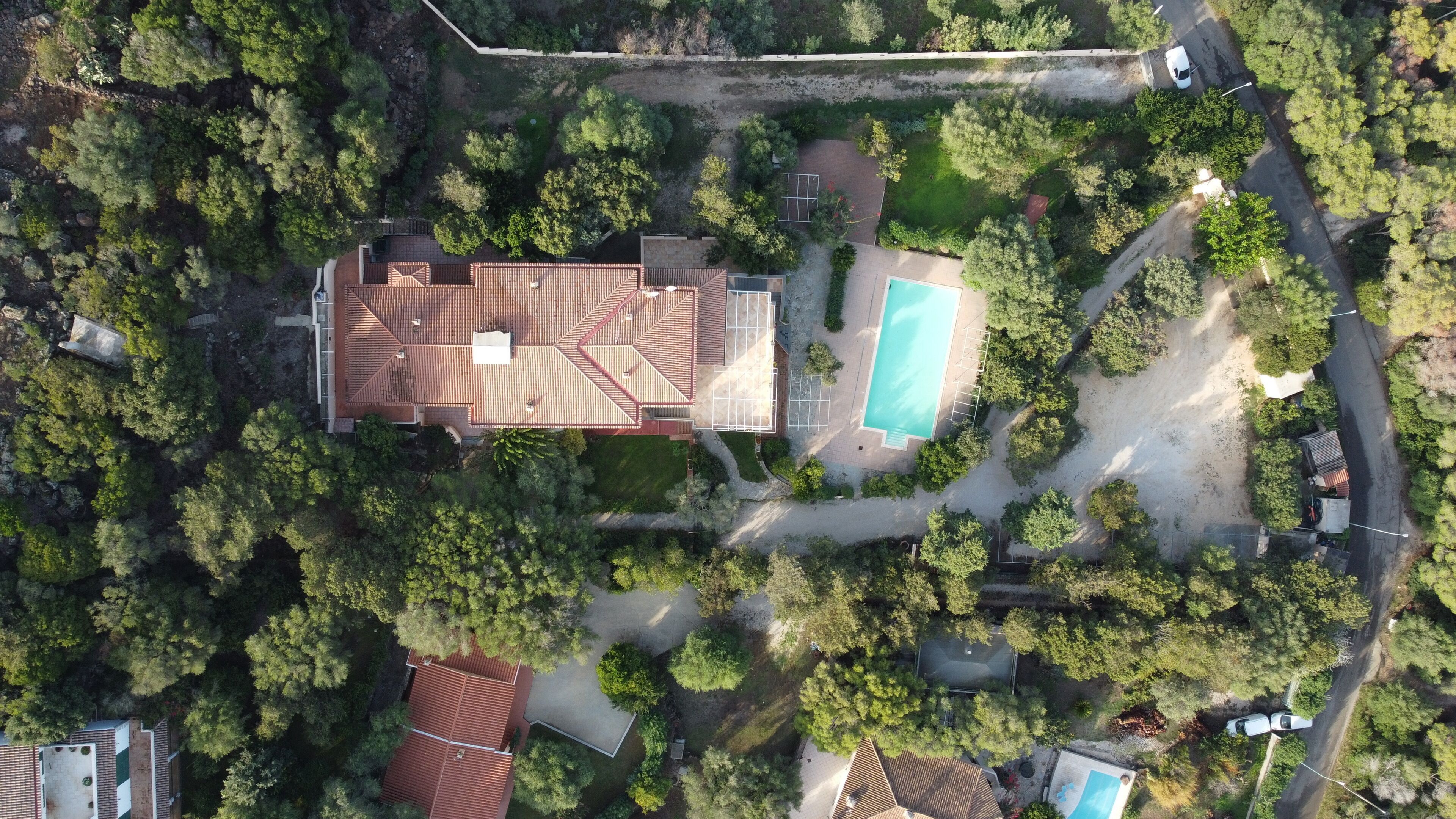 Vista aérea de una zona residencial con una casa grande, una piscina y vegetación circundante.