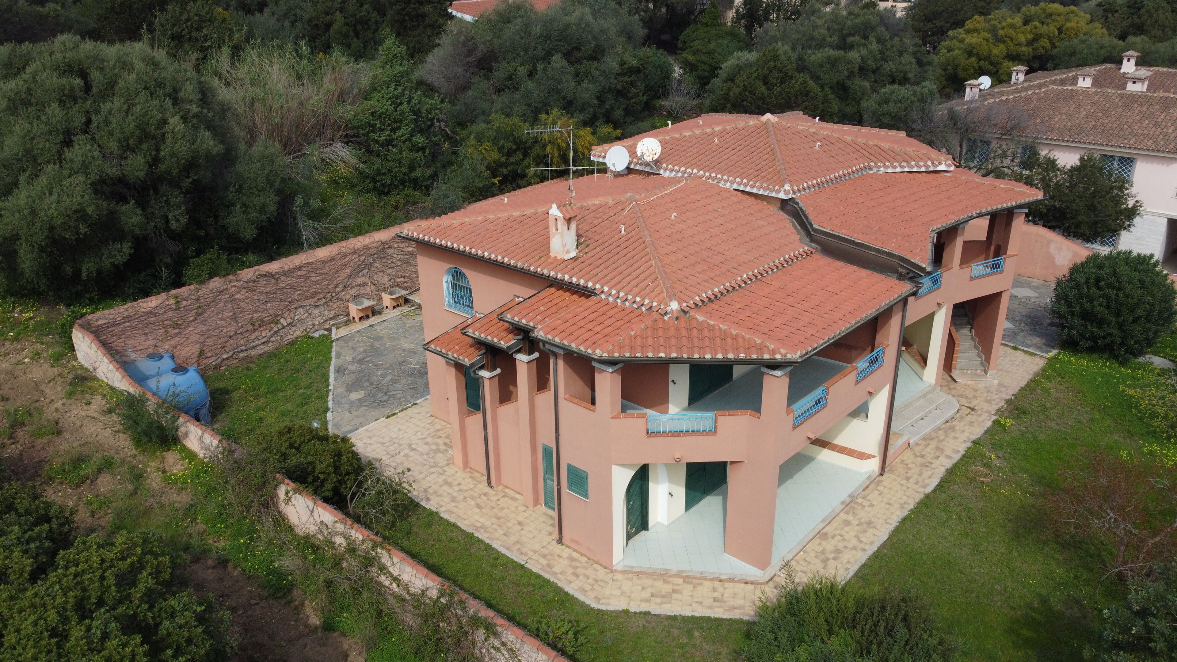 A multi-story house with a tiled roof, satellite dishes, and a stone wall.