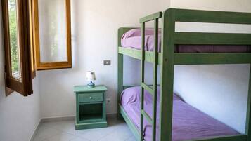 A bunk bed with a nightstand and a lamp, a window with a wooden frame, and a wall-mounted mirror.