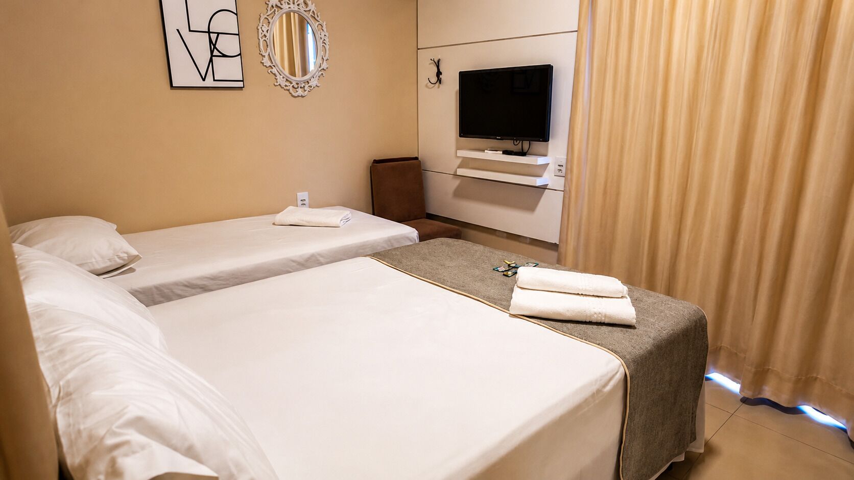Habitación de hotel con dos camas, un televisor, un espejo y una cortina.