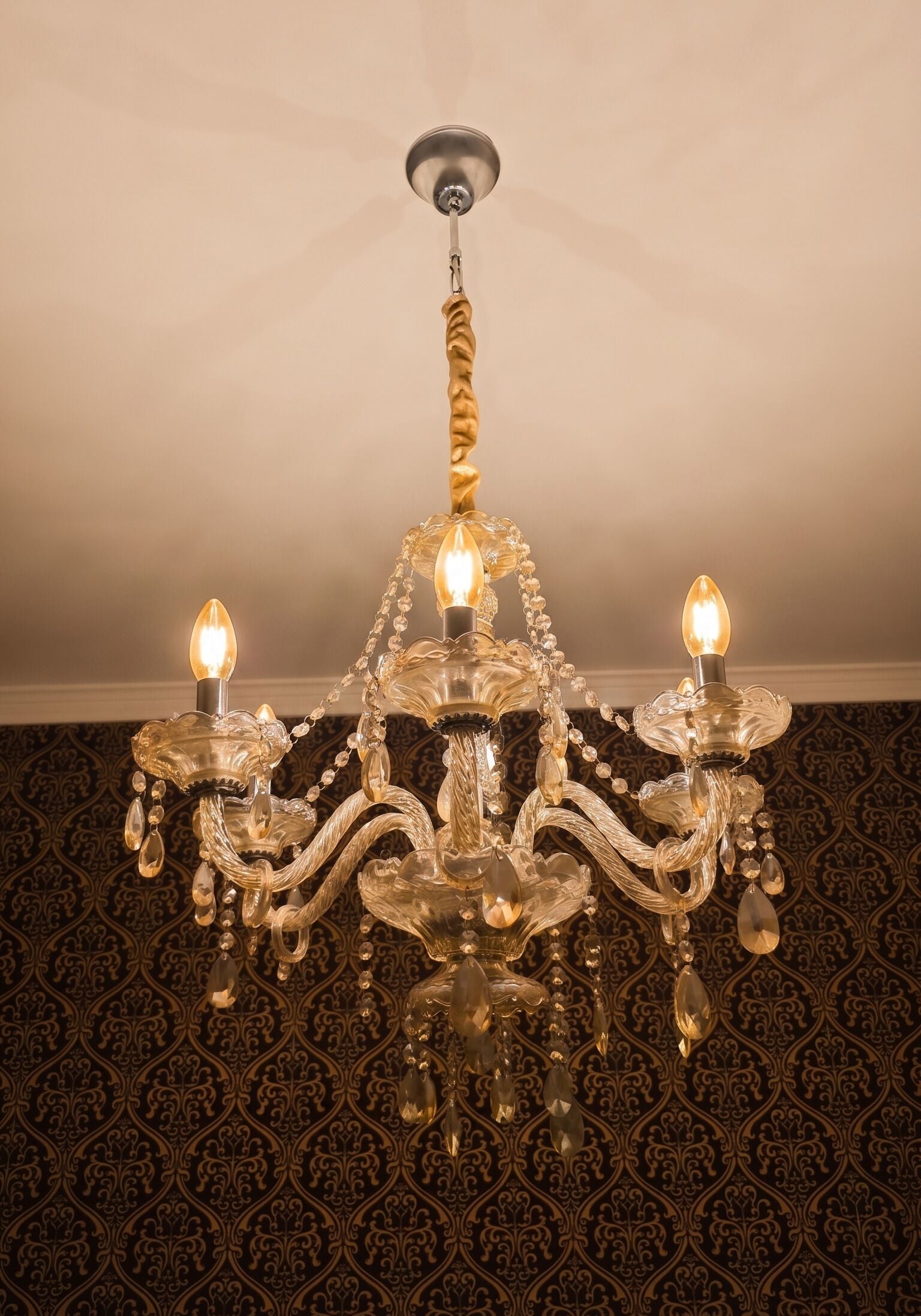 A chandelier with three lights, a twisted metal handle, and crystal decorations.