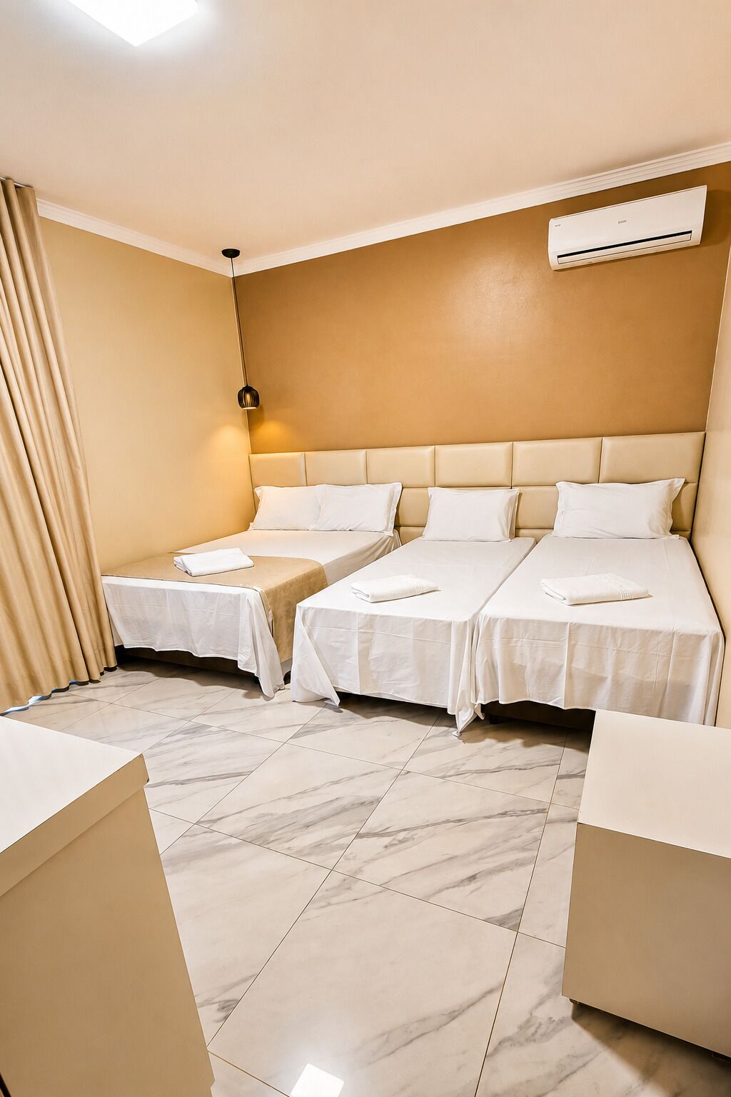 Habitación de hotel con dos camas, una lámpara en el techo, un equipo de aire acondicionado y piso de baldosas de mármol.